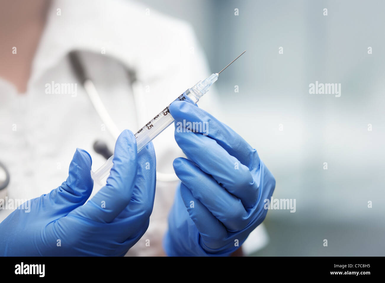 Syringe held by a doctor with stethoscope and blue gloves preparing a shot for flu or sedative Stock Photo