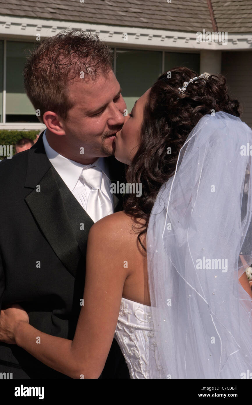 Couple's first kiss during Catholic wedding ceremony held outside during sunny summer day Stock Photo