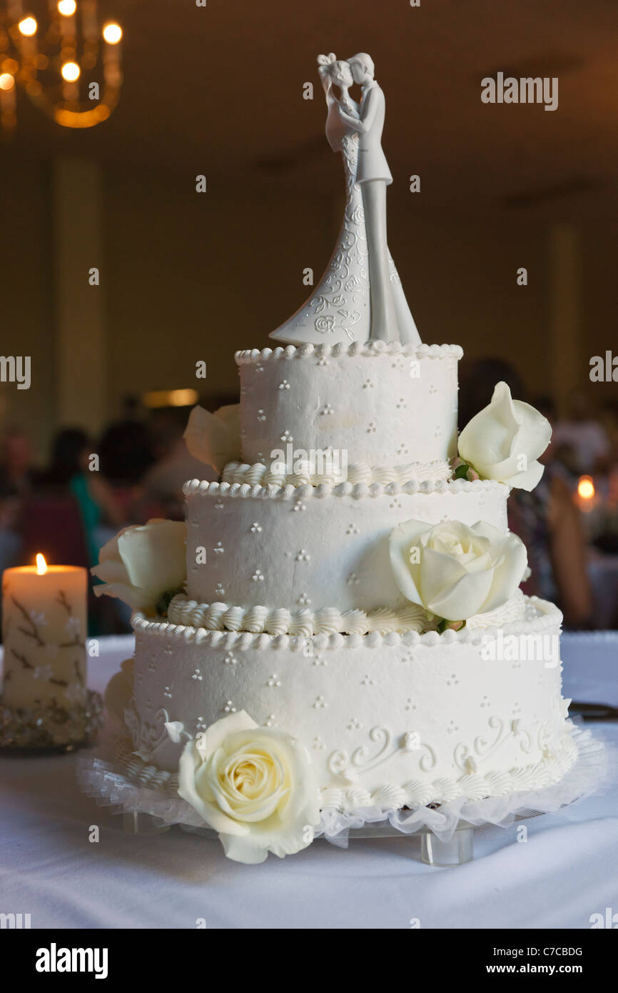 Multi layered wedding cake decorated with white frosting, yellow roses and bride and groom figurines topper Stock Photo