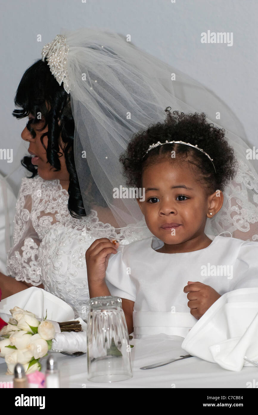 African American bride wearing wedding dress and veil sitting with her daughter at a table during wedding reception Stock Photo