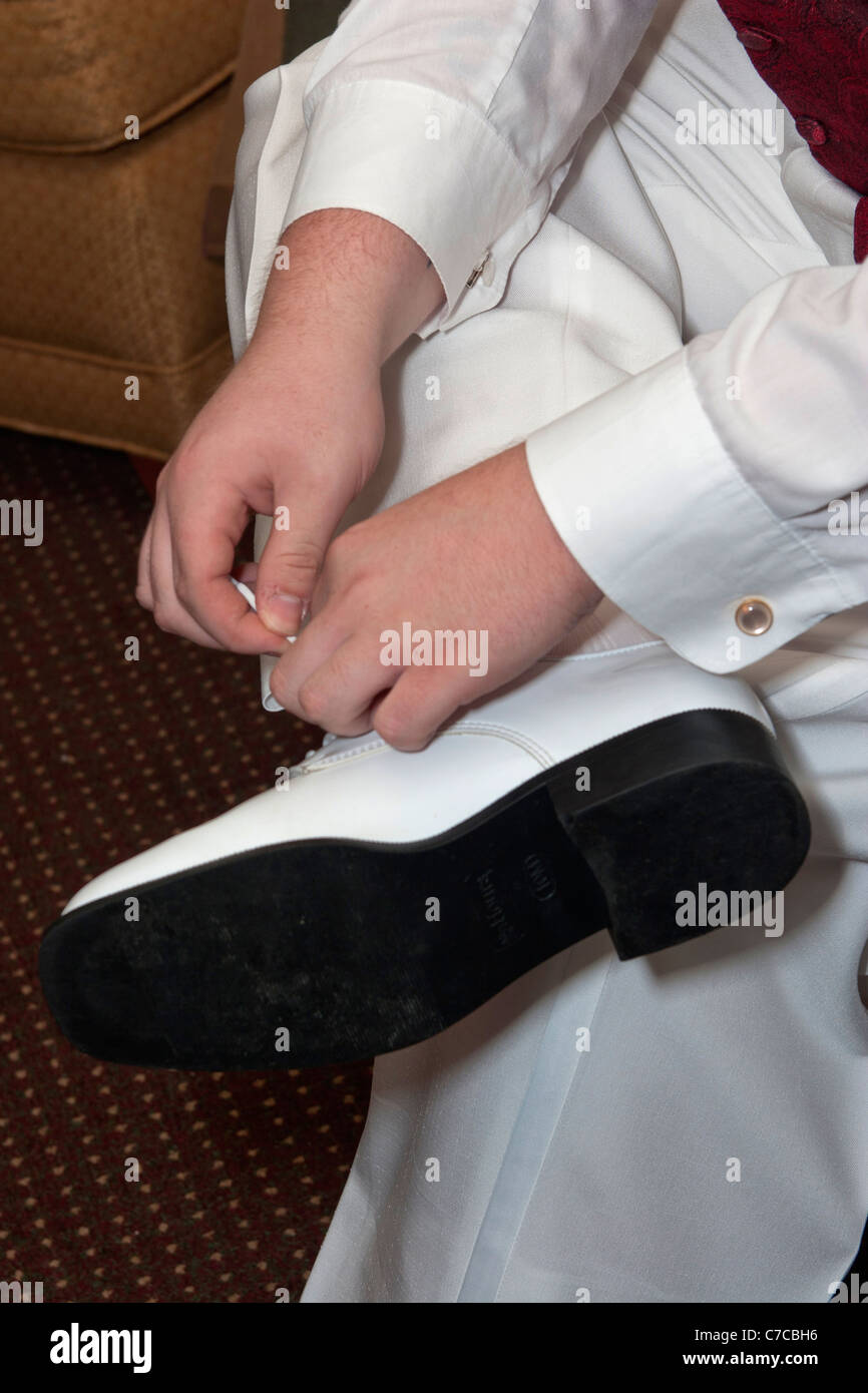 Groom dressed in white tuxedo pants tying his white shiny shoes Stock Photo