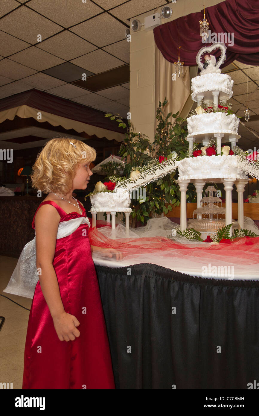 A flower girl looking at large multi-tiered cake with lit fountain under neath and bride and broom figurines topper Stock Photo