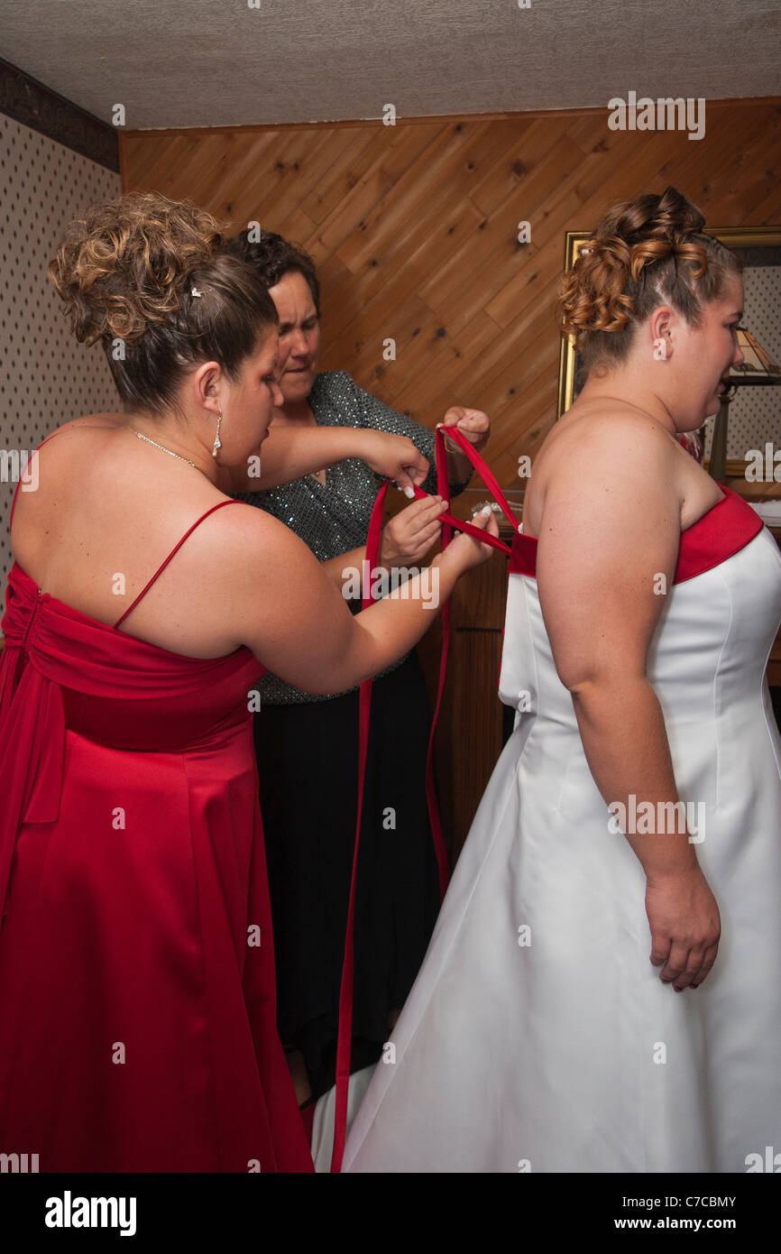 Bridesmaid and the mother helping the bride with dressing - tying a ribbon on a back of the dress Stock Photo