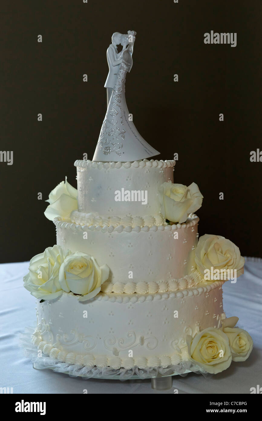 Large multi-tiered cake decorated with yellow frosting with bride and broom figurines topper displayed on table during reception Stock Photo