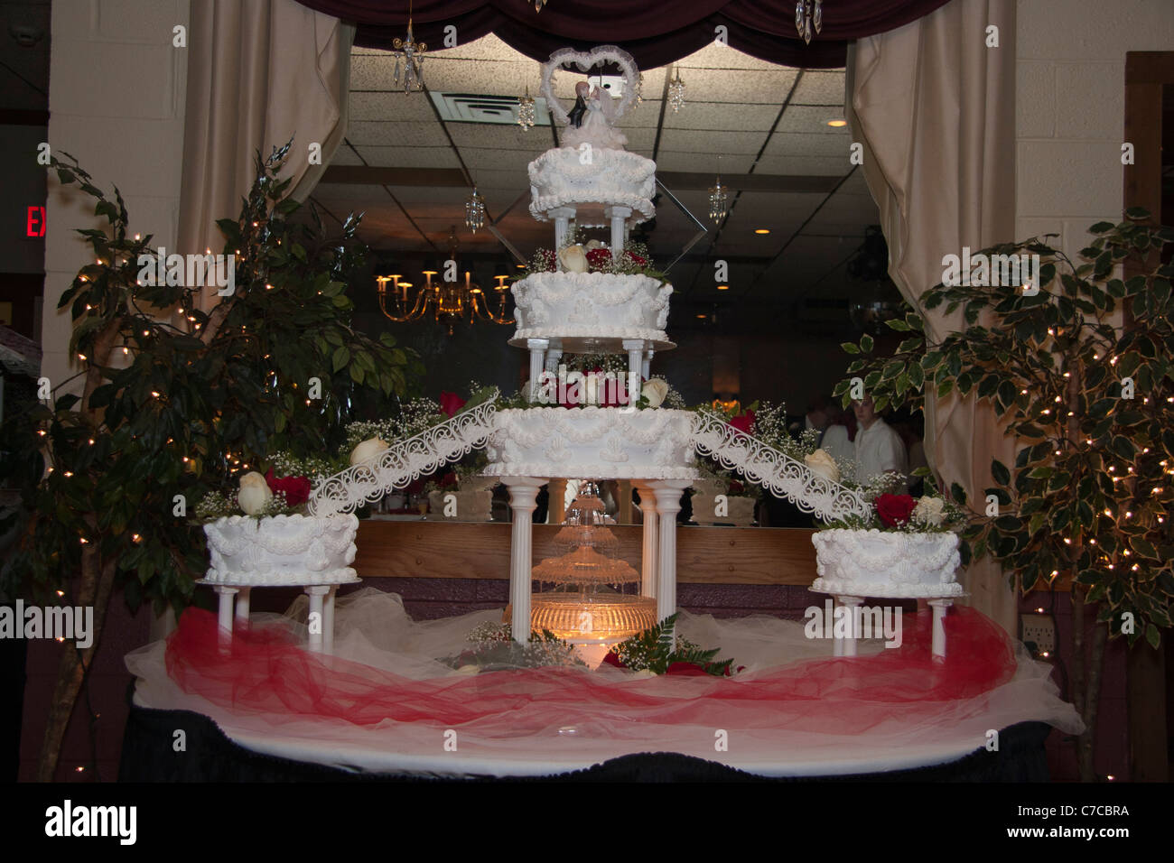 Large multi-tiered cake with lit fountain under neath and bride and broom figurines topper displayed on table during reception Stock Photo