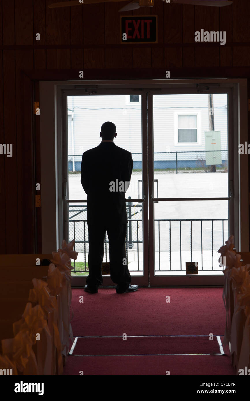 A silhouette of a man in the church standing in front of bright entry glass doors Stock Photo