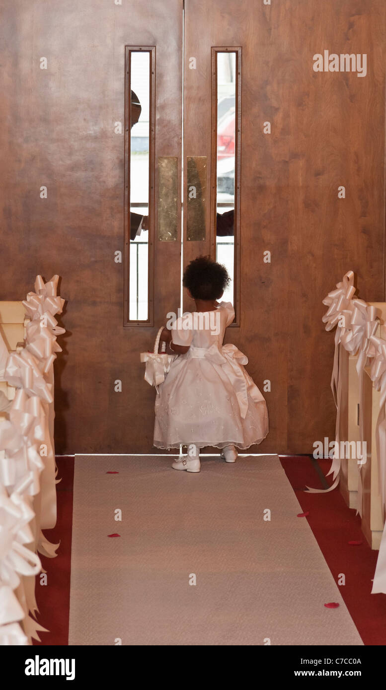 A little African-American flower girl walking away towards the entry door at the church during a wedding ceremony Stock Photo