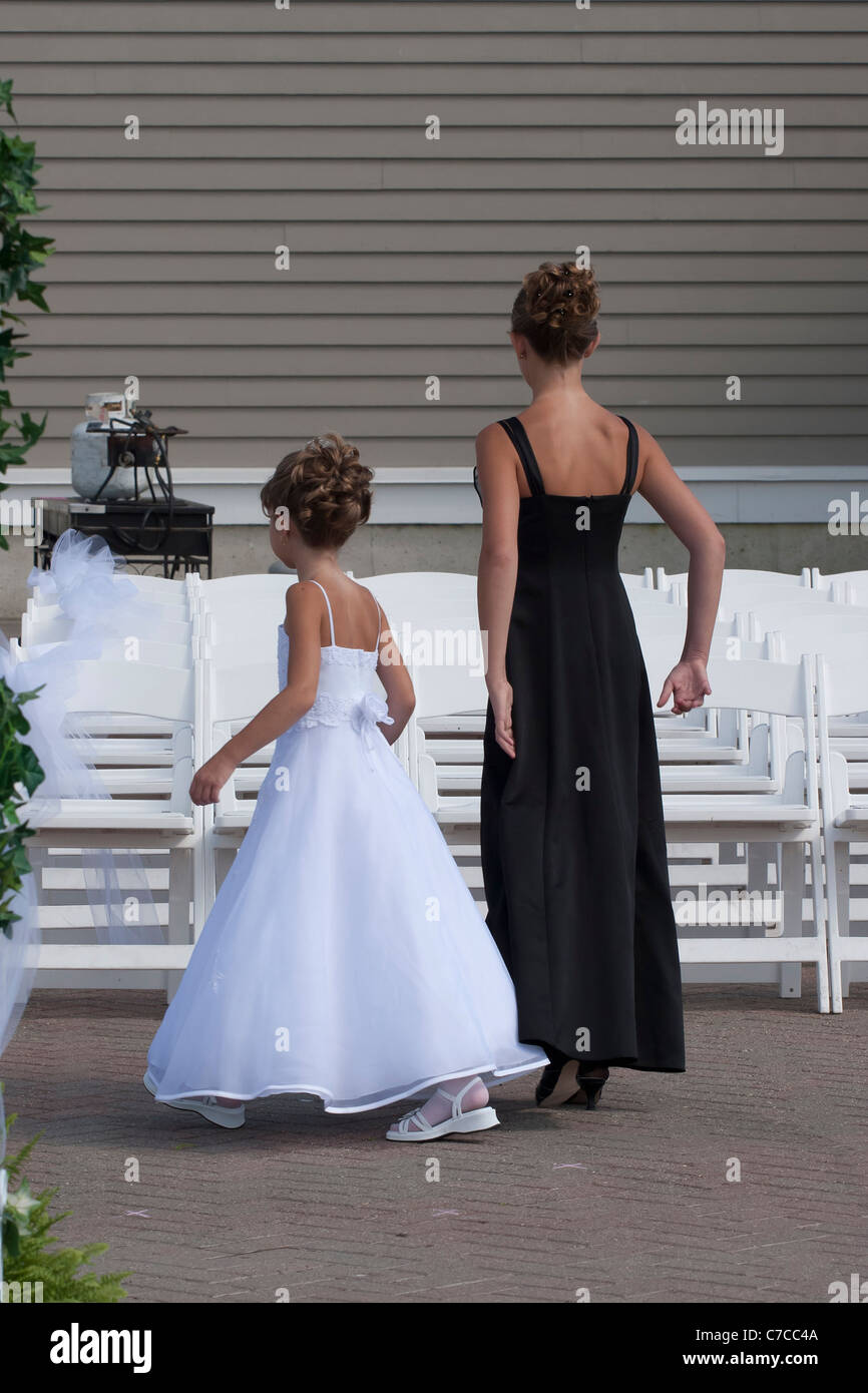 Flower girl with another young girl wedding guest in front of rows of white chairs set up for outdoors wedding Stock Photo