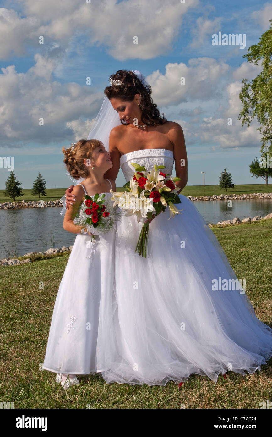 A portrait of newly wed bride and a flower girl looking into each other eyes with blue sky and white puffy clouds in background Stock Photo