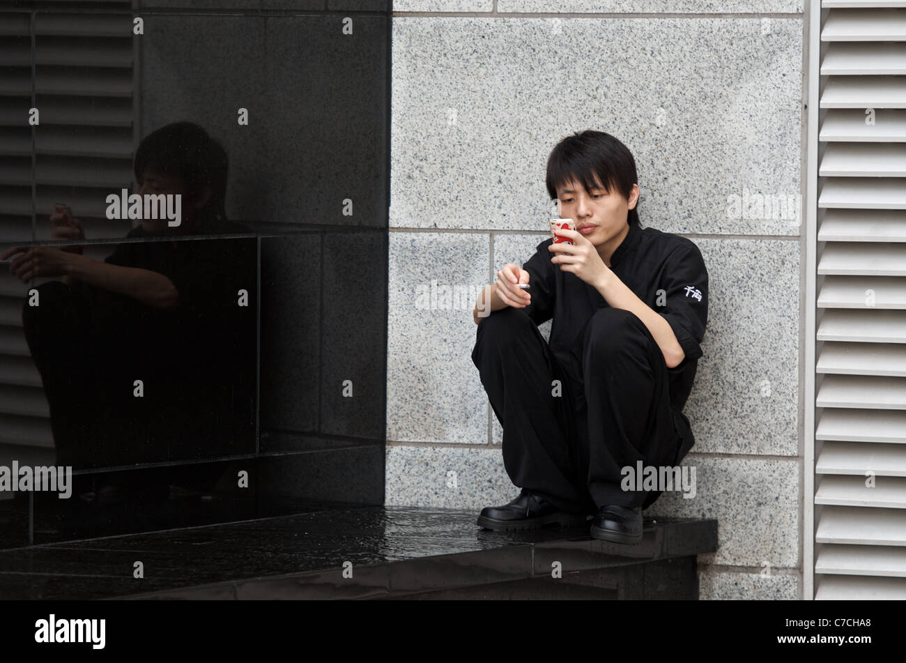 A restaurant worker taking a cigarette break and playing with his mobile smartphone. Stock Photo