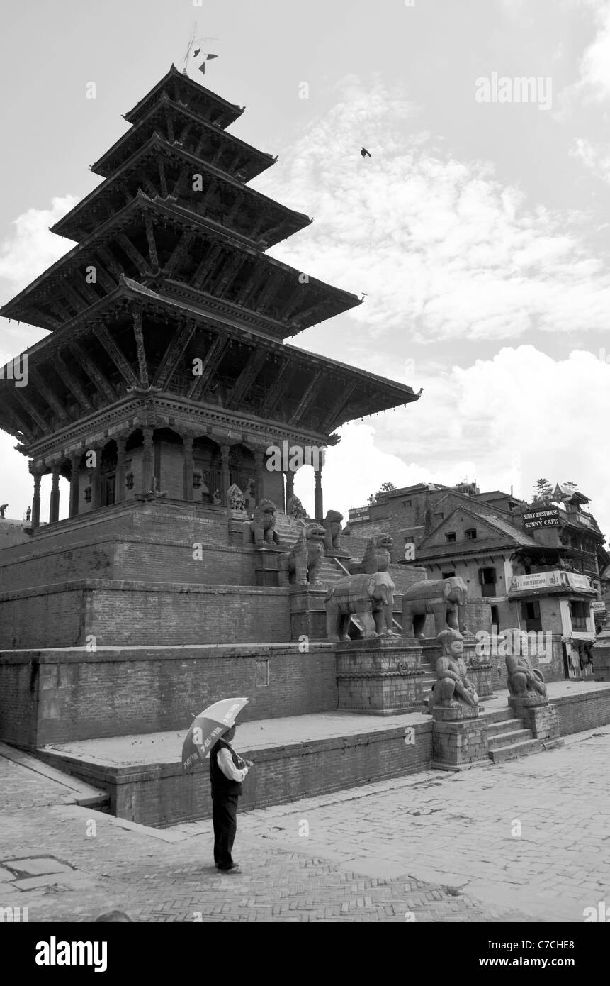 A man with an umbrella in front of a pagoda-style temple with large statues of men and animals, Durbar Square, Bhaktapur, Nepal Stock Photo