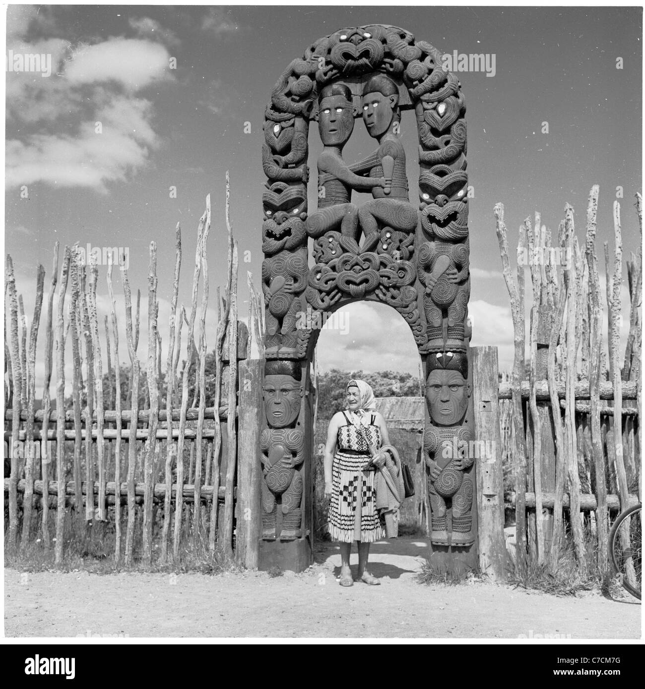 New Zealand. 1950s. Historical view of a Maori woman standing at entrance to national park entrance showing carved figures. Stock Photo