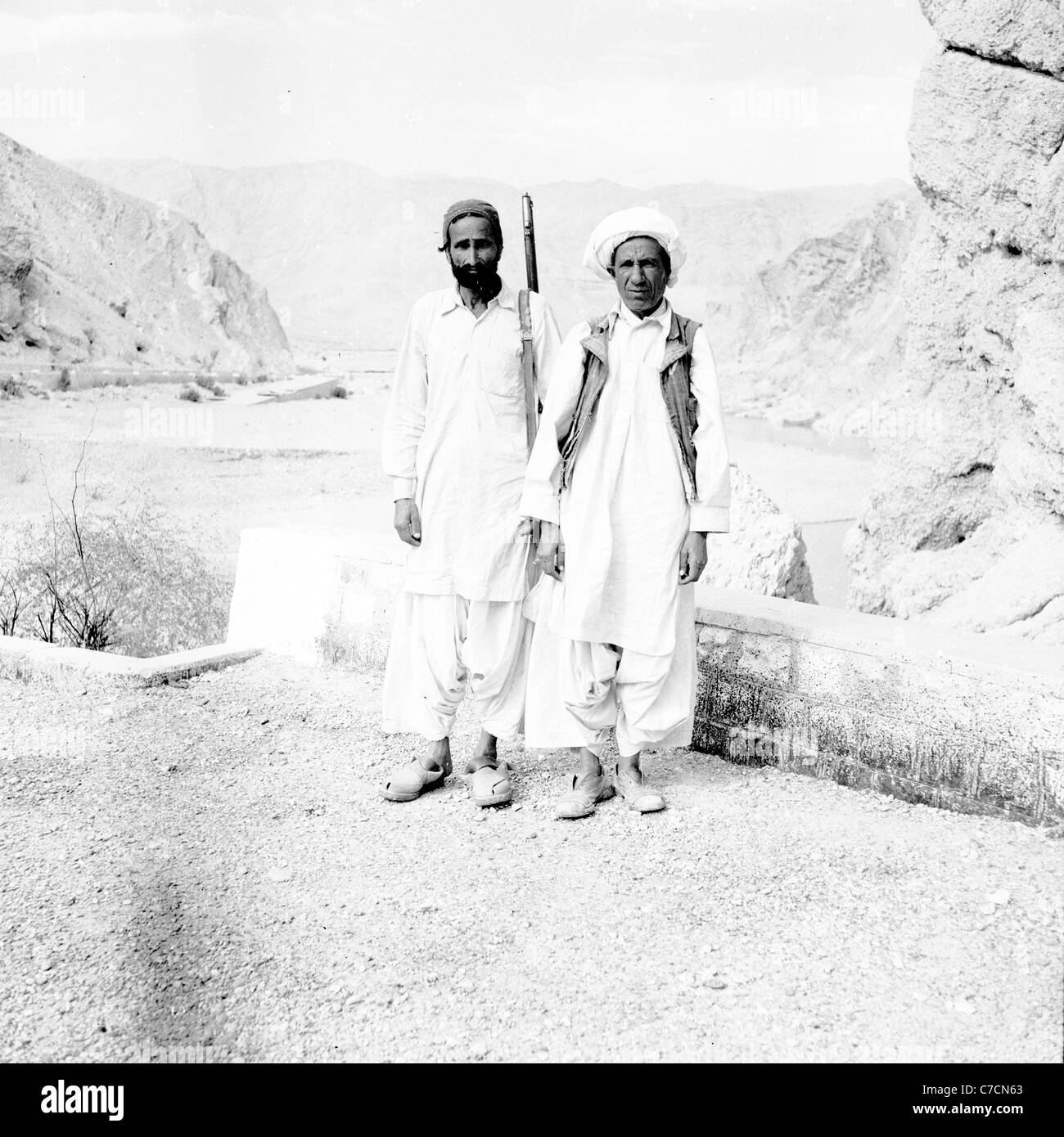 Two tribesmen or pashtuns, one armed with rifle, standing at the Bolan Pass, Pakistan. Taken in 1950s by J. Allan Cash. Stock Photo