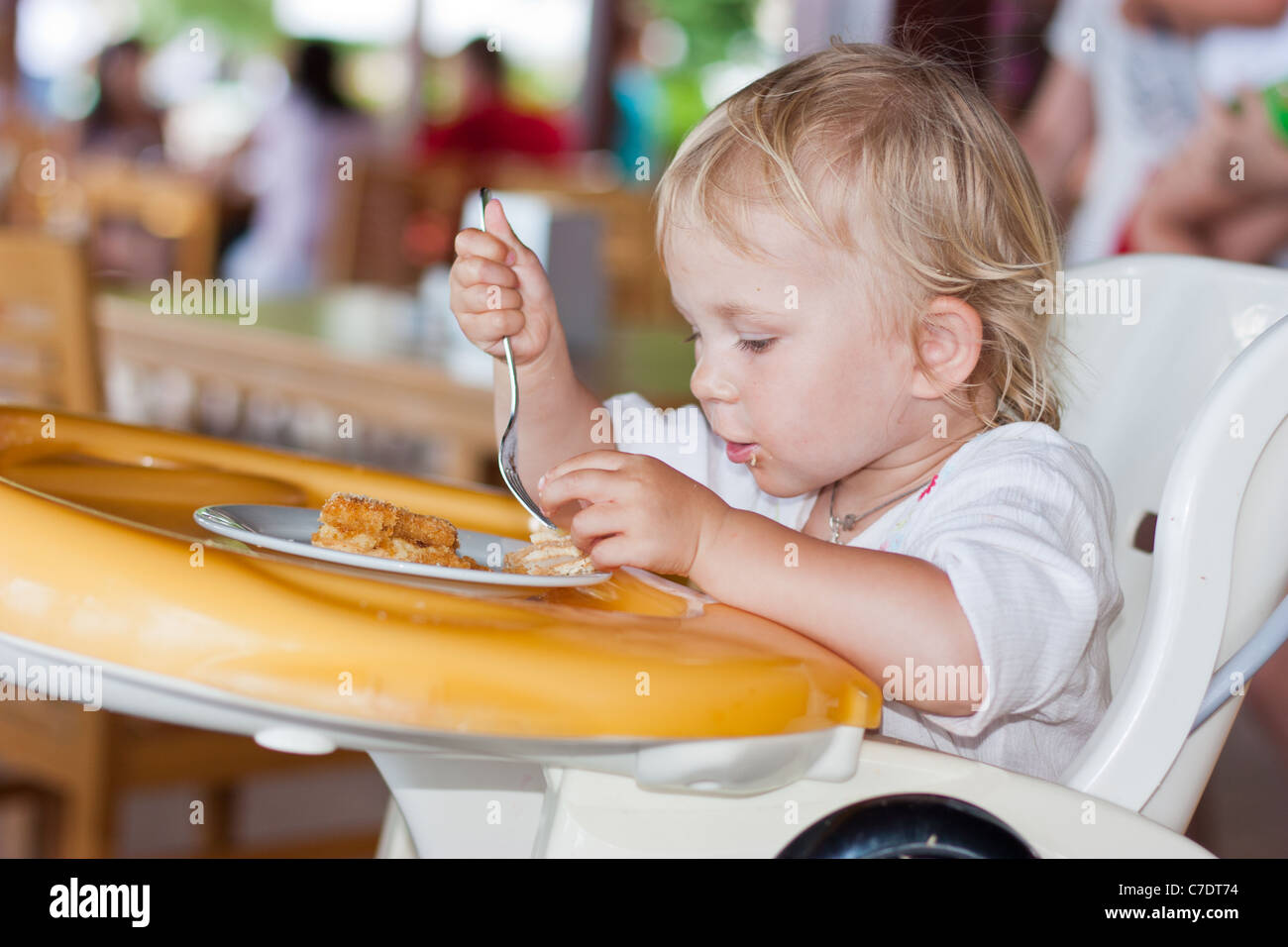 Cute child eating with a fork in a chair Stock Photo - Alamy