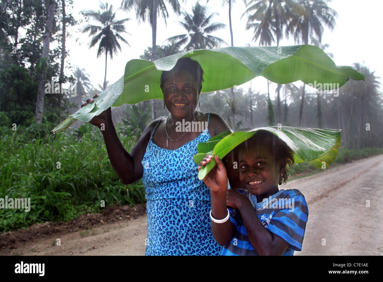 Mother and child using banana leaf as umbrella against pouring rain. Jungle of Bougainville Island, Papua New Guinea Stock Photo