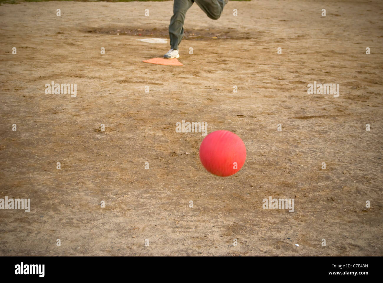 A red kickball rolls toward home plate after it is pitch the person pictured here on plate is