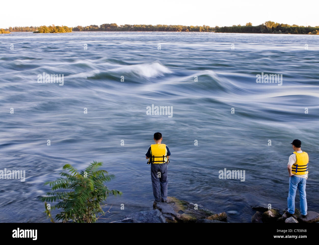 2 men wearing yellow lifesaving jackets fishing in Saint Lawrence river, Stock Photo