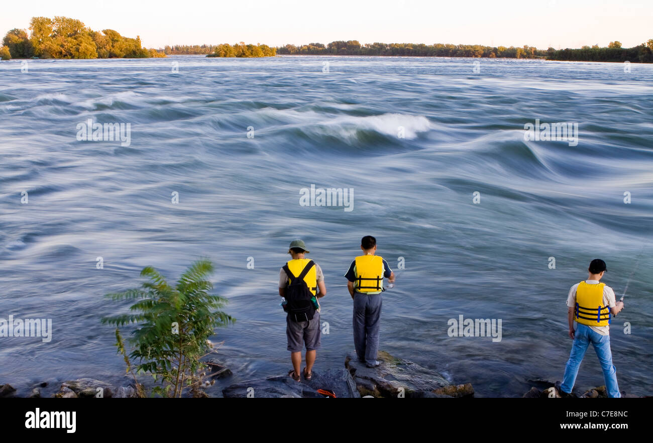 3 men wearing yellow lifesaving jackets fishing in Saint Lawrence river Stock Photo