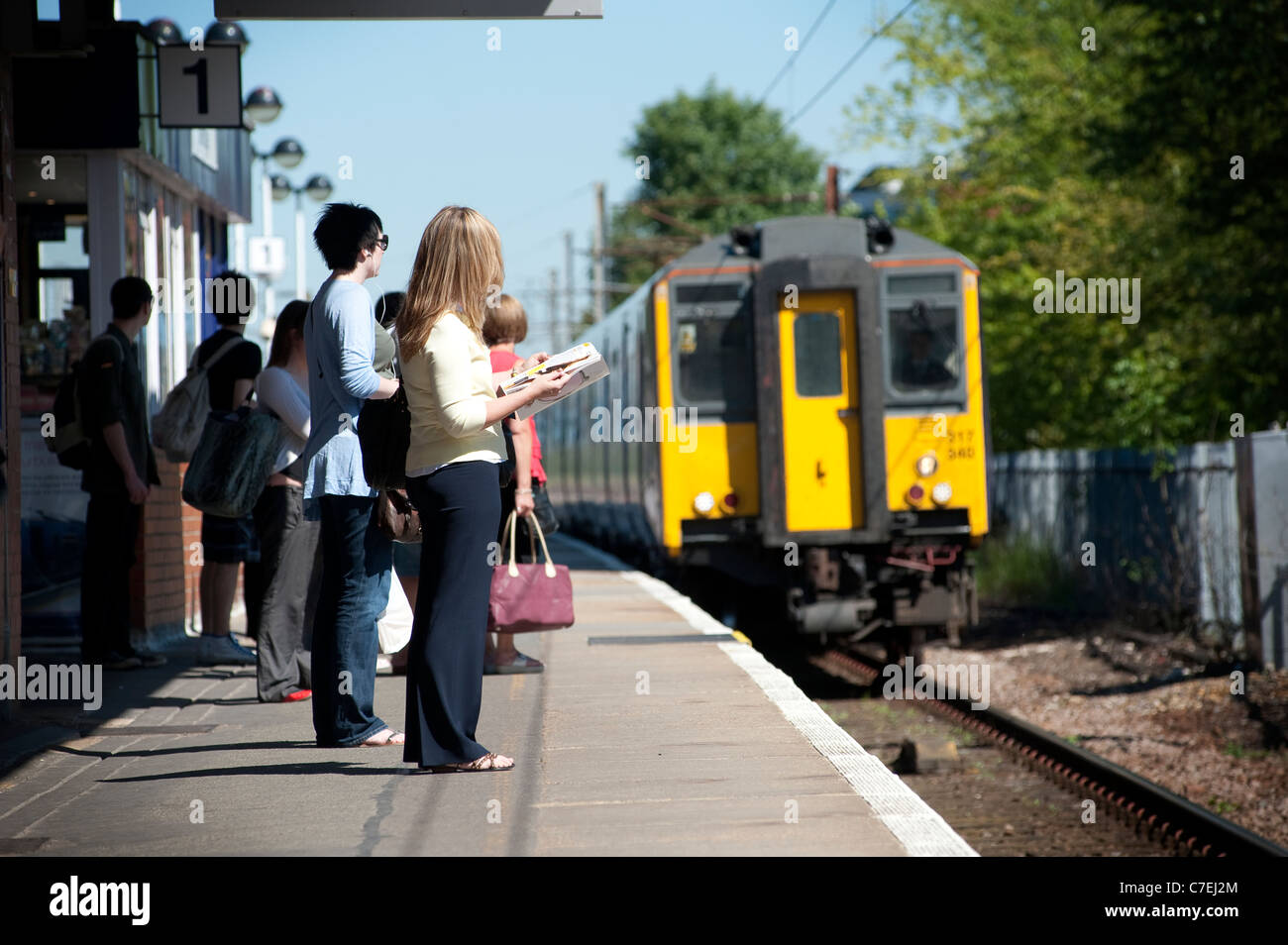 Passengers waiting on a railway station platform as a train approaches. Stock Photo