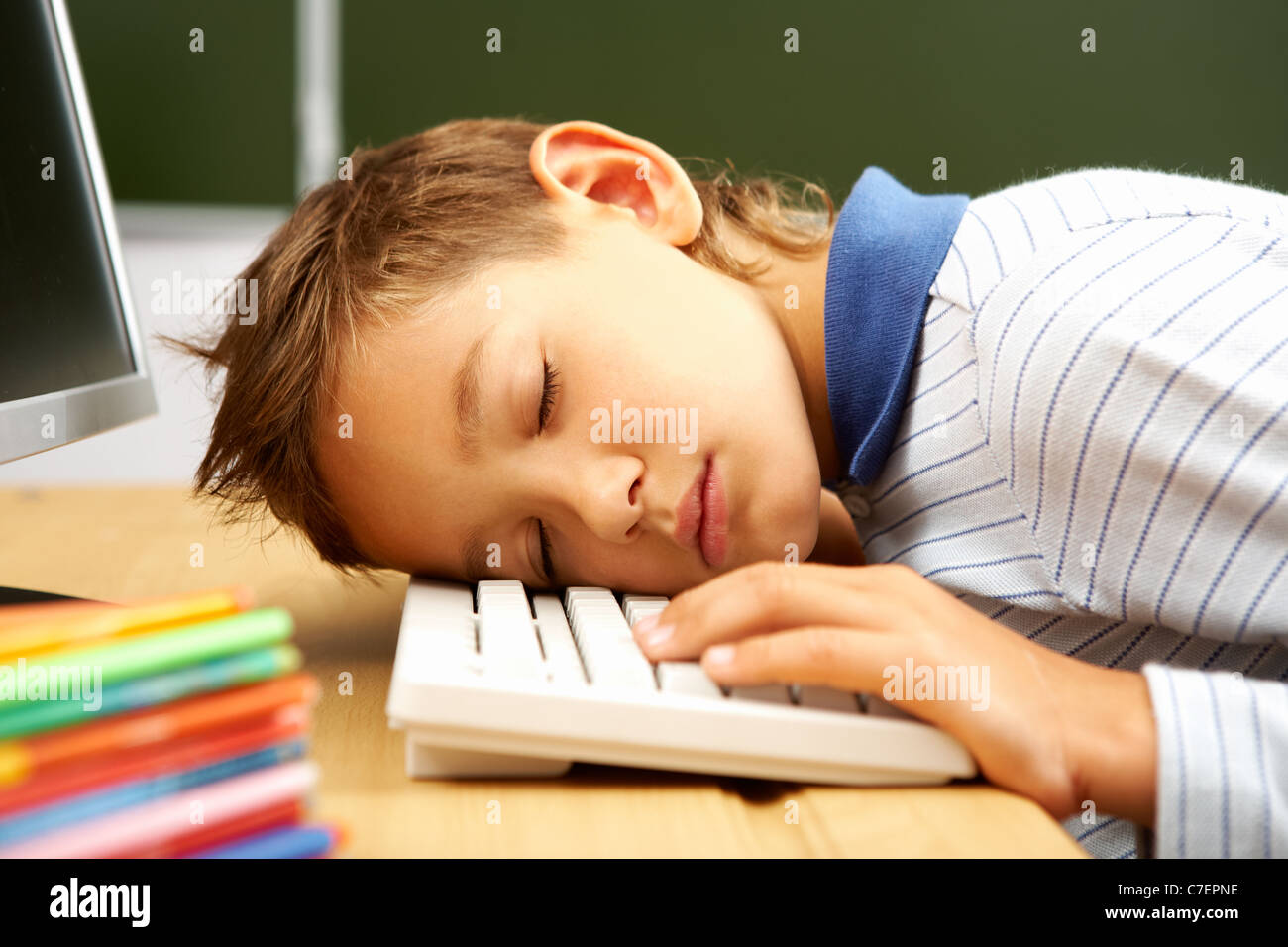 Portrait of cute lad sleeping with his head on computer keyboard in