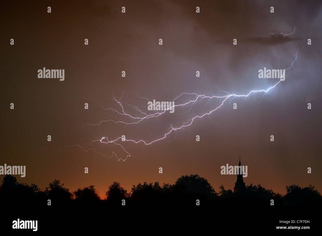 Forked lightning during thunderstorm at night over church tower and trees, Belgium Stock Photo
