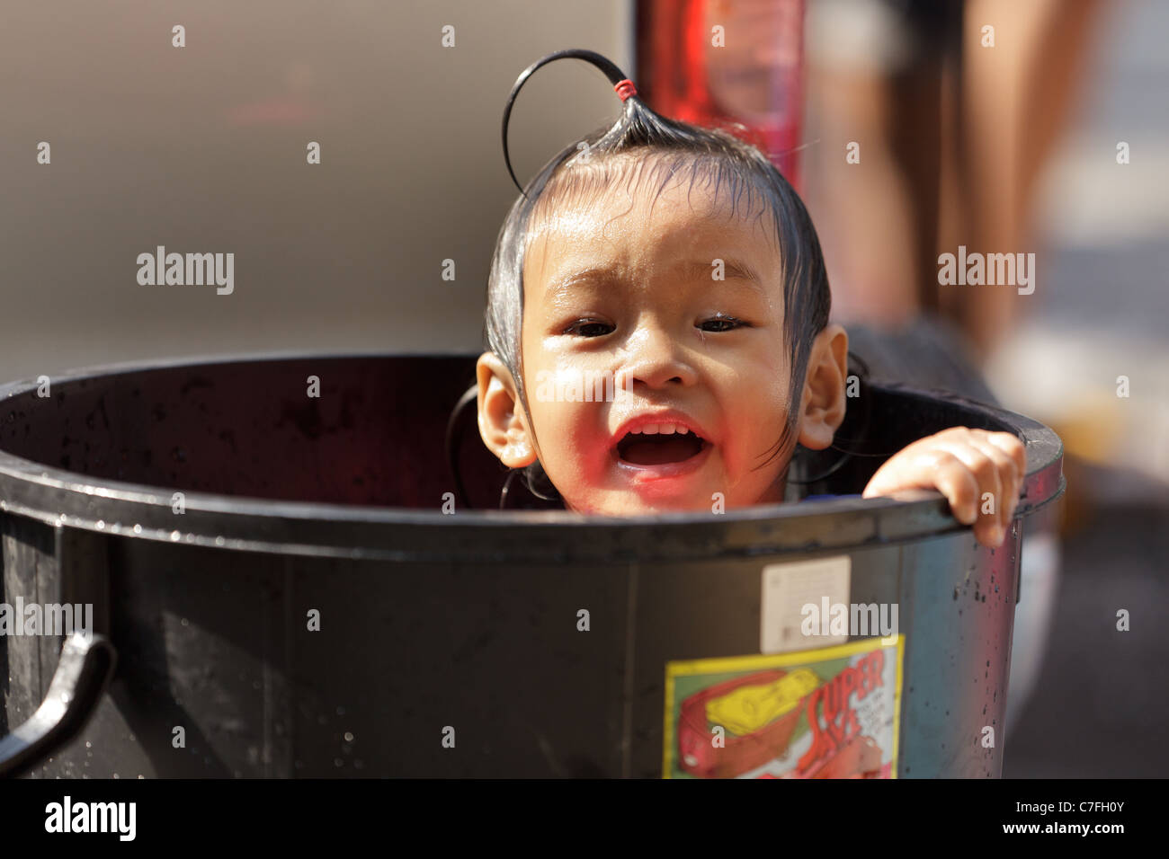 Thai kid  taking a bath in platic bin during song kran buddhist new year festival in silom road, Bangkok, Thailand Stock Photo