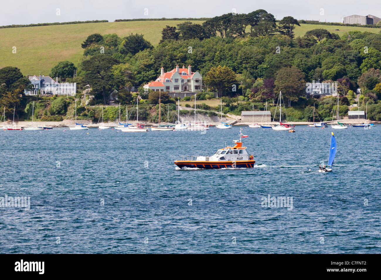 A pilot boat going up the River Fal opposite Falmouth, passing expensive properties at Flushing, Cornwall Stock Photo