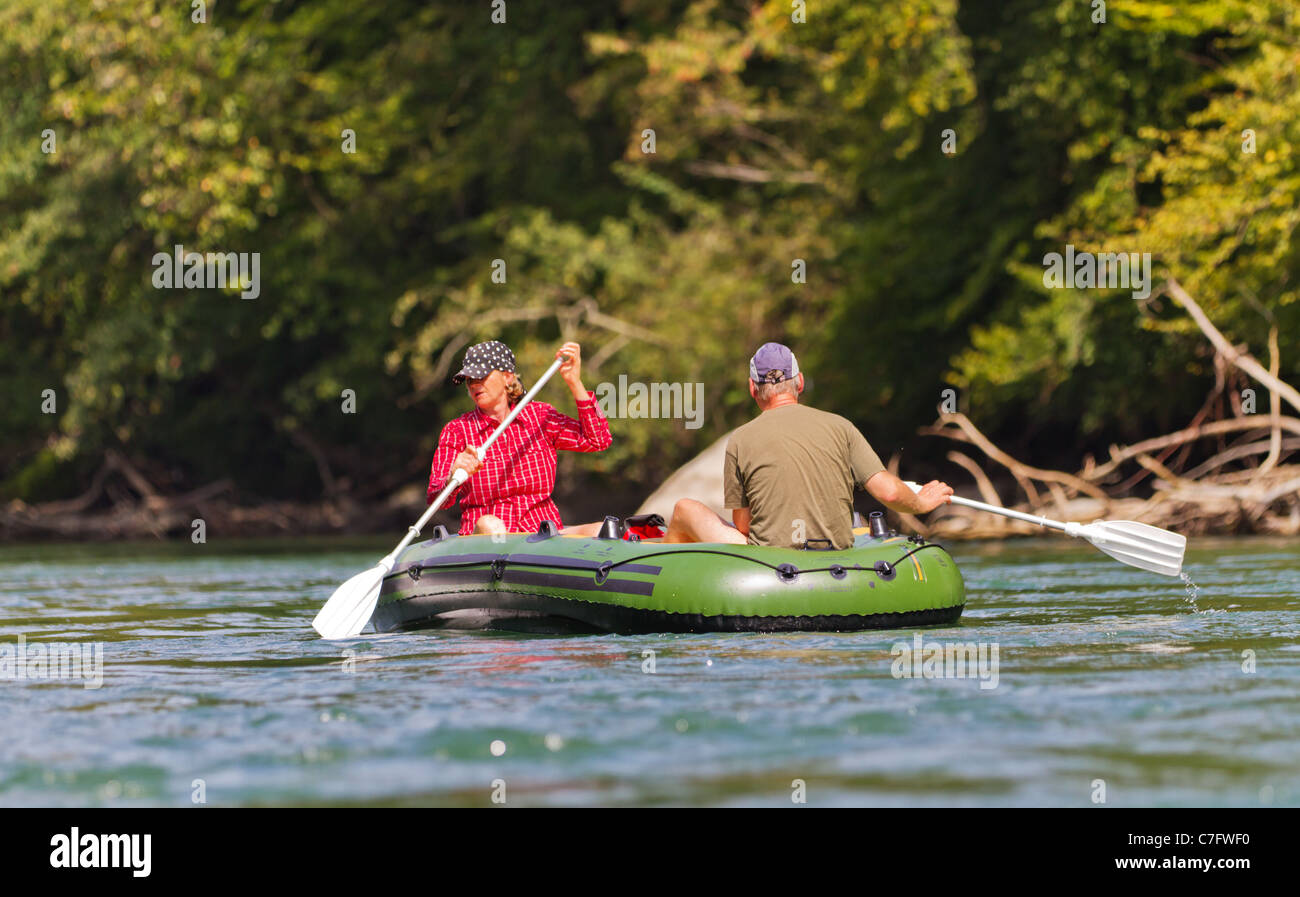 middle aged couple sits in rubber dinghy paddle in hand rowing together on a river in pretty natural summer settings Stock Photo
