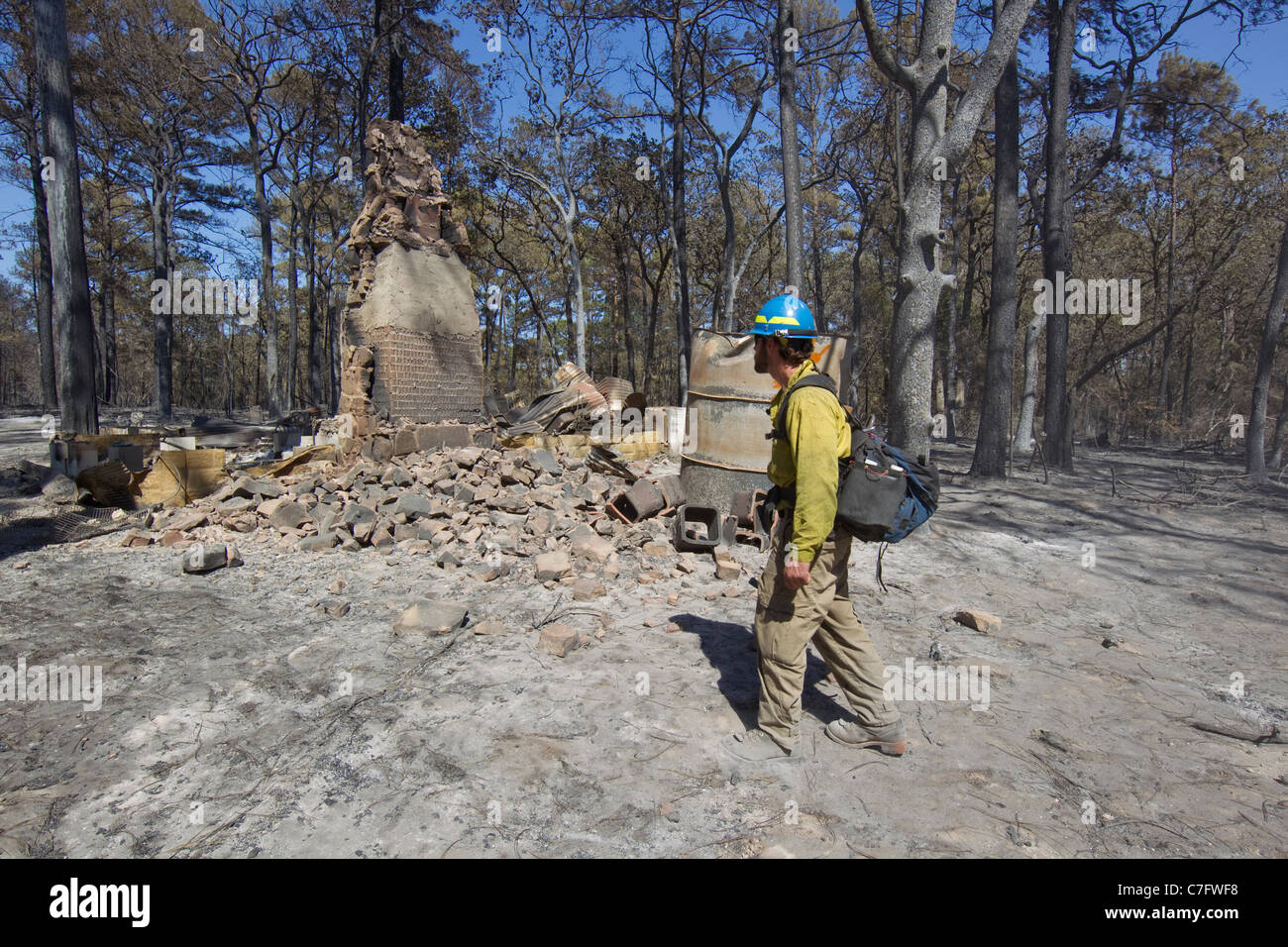 Firefighter wearing safety gear looks for hot spots in heavily forested residential area hit by wildfire near Bastrop Texas Stock Photo