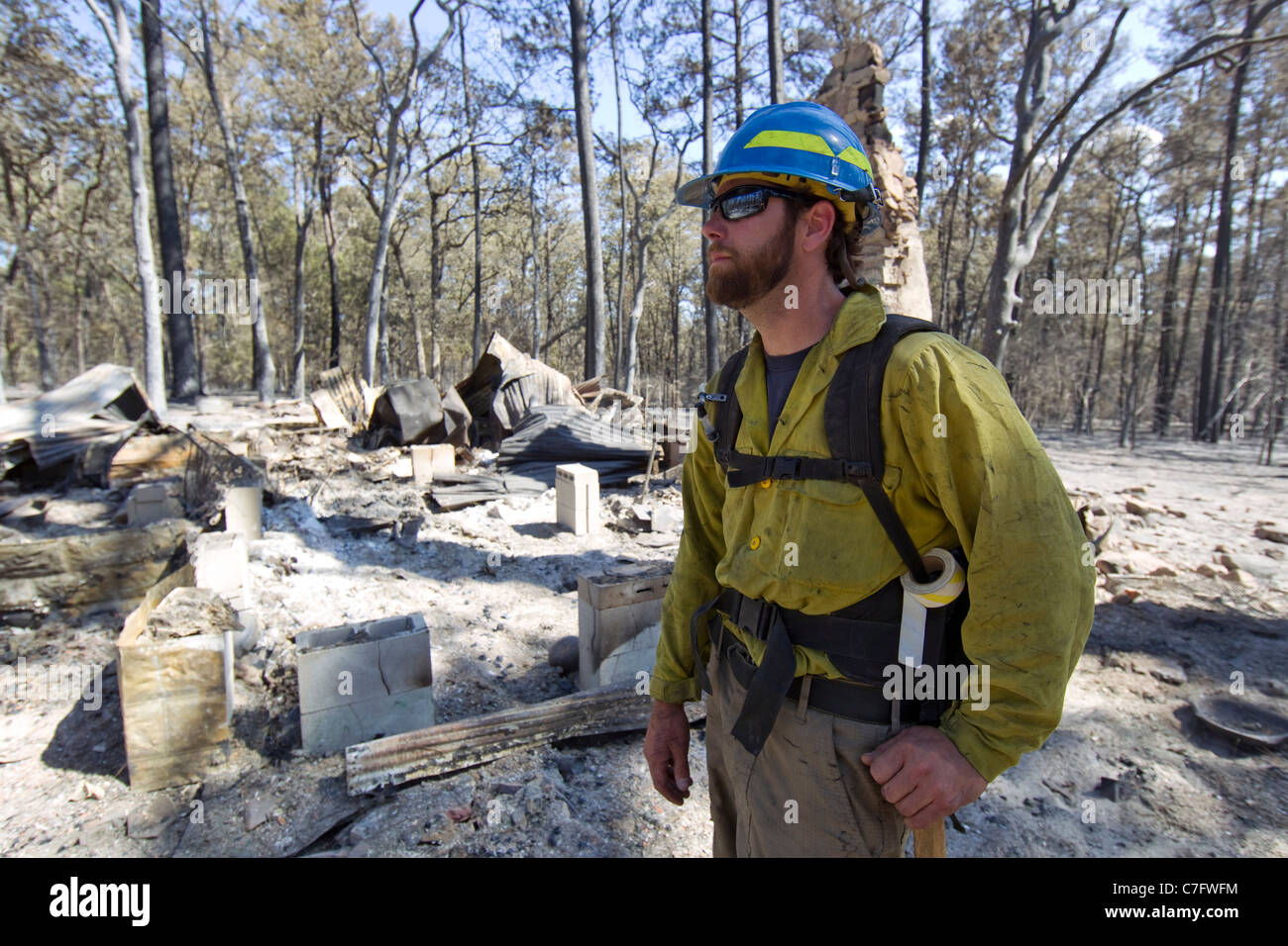 Firefighter wearing safety gear looks for hot spots in heavily forested residential area hit by wildfire near Bastrop Texas Stock Photo