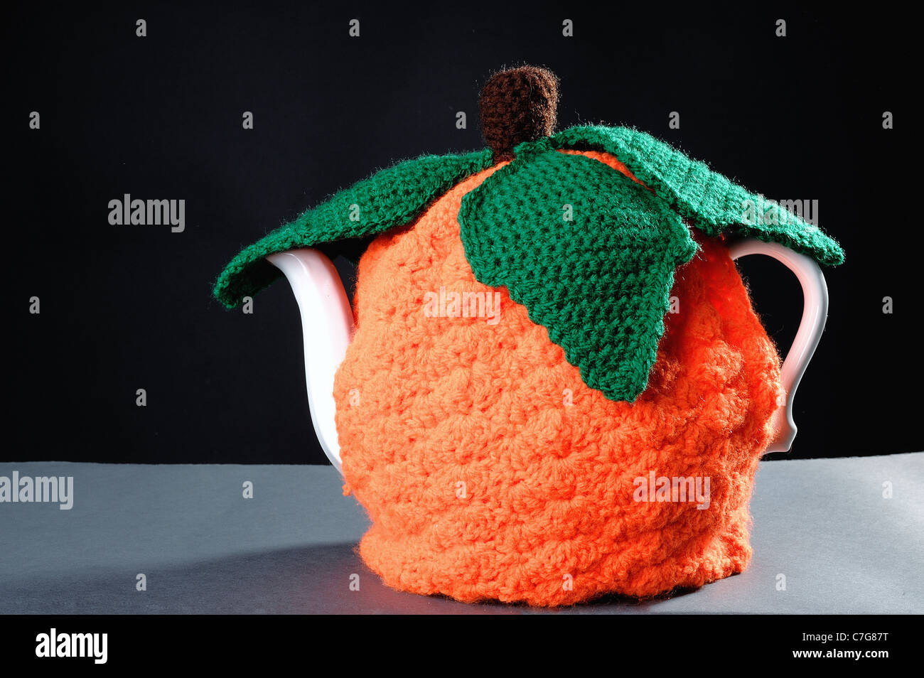 Jack o lantern pumpkin tea cosy on a black and grey gray background made for Halloween Stock Photo