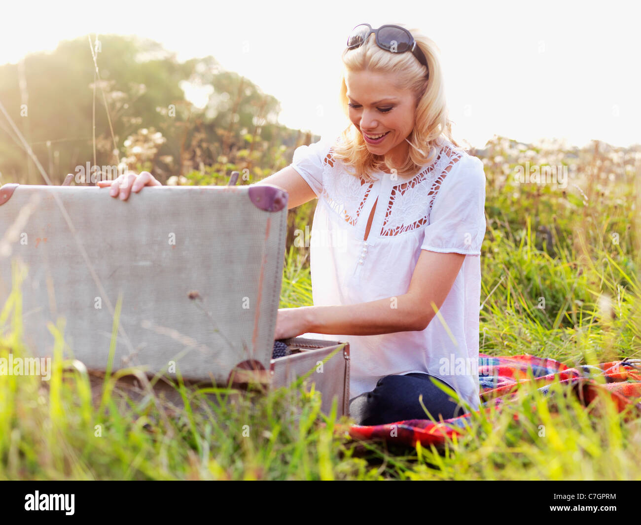 A woman sitting in the grass rummaging through an open suitcase Stock Photo