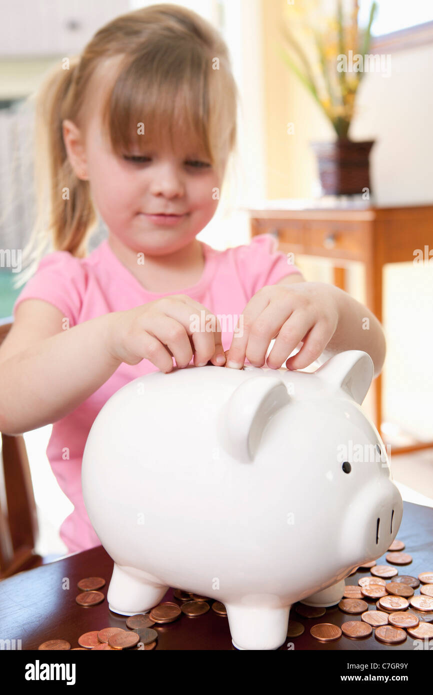 A girl putting coins into a piggy bank Stock Photo - Alamy