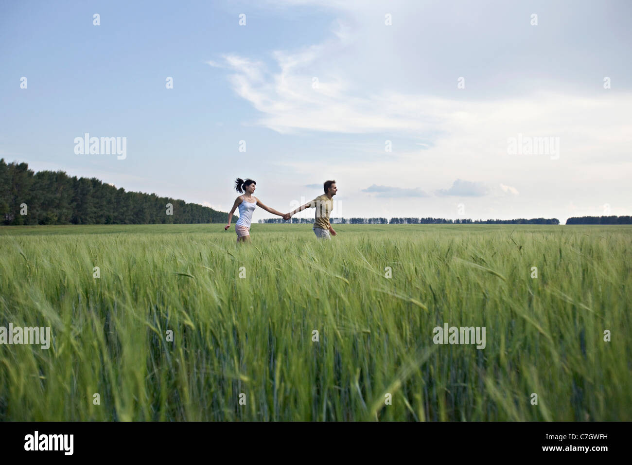 A man and woman holding hands and running through a wheat field Stock Photo