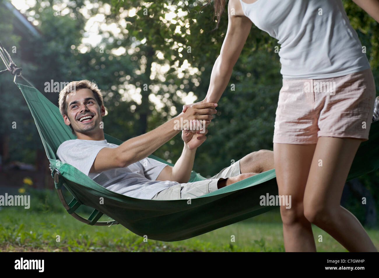 A man lying in a hammock pulling his girlfriend down Stock Photo
