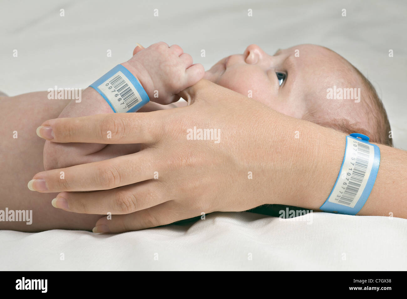 A baby holding her mother's thumb, both wearing hospital ID bracelets Stock Photo
