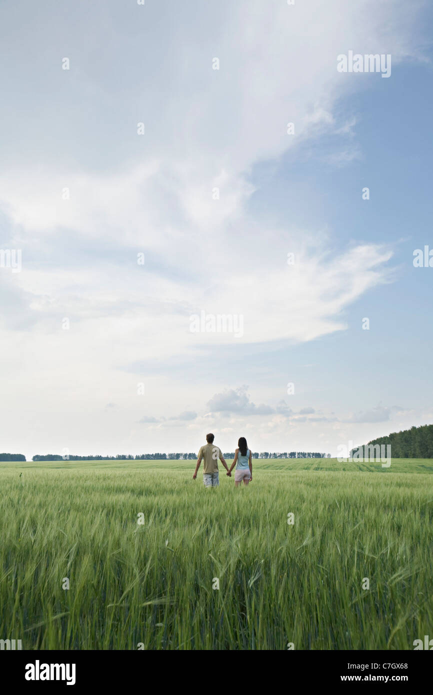 A man and woman walking hand in hand through a remote field Stock Photo