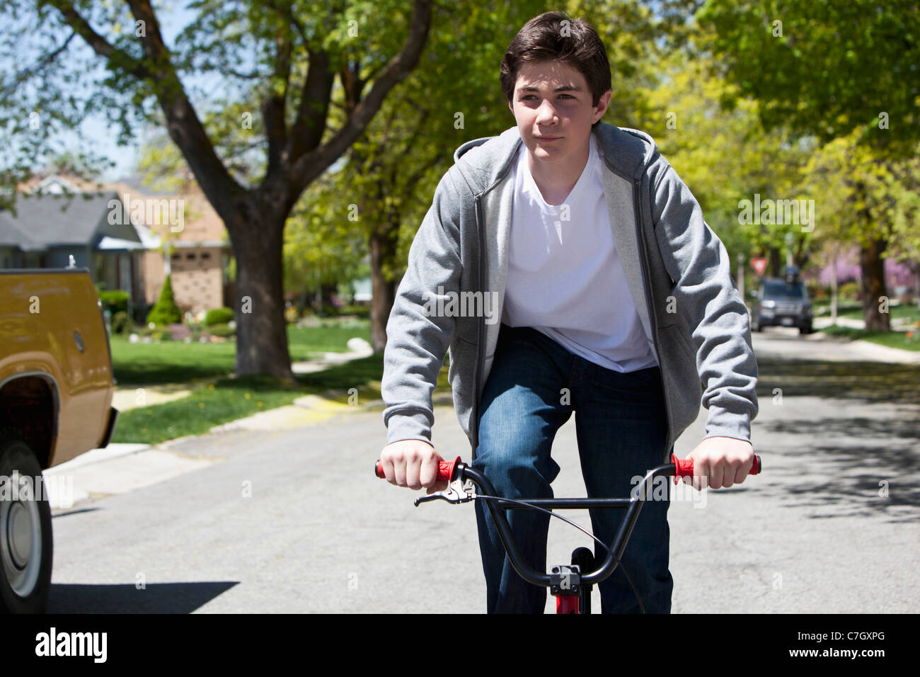 Boy stands while riding bike with a content facial expression Stock Photo