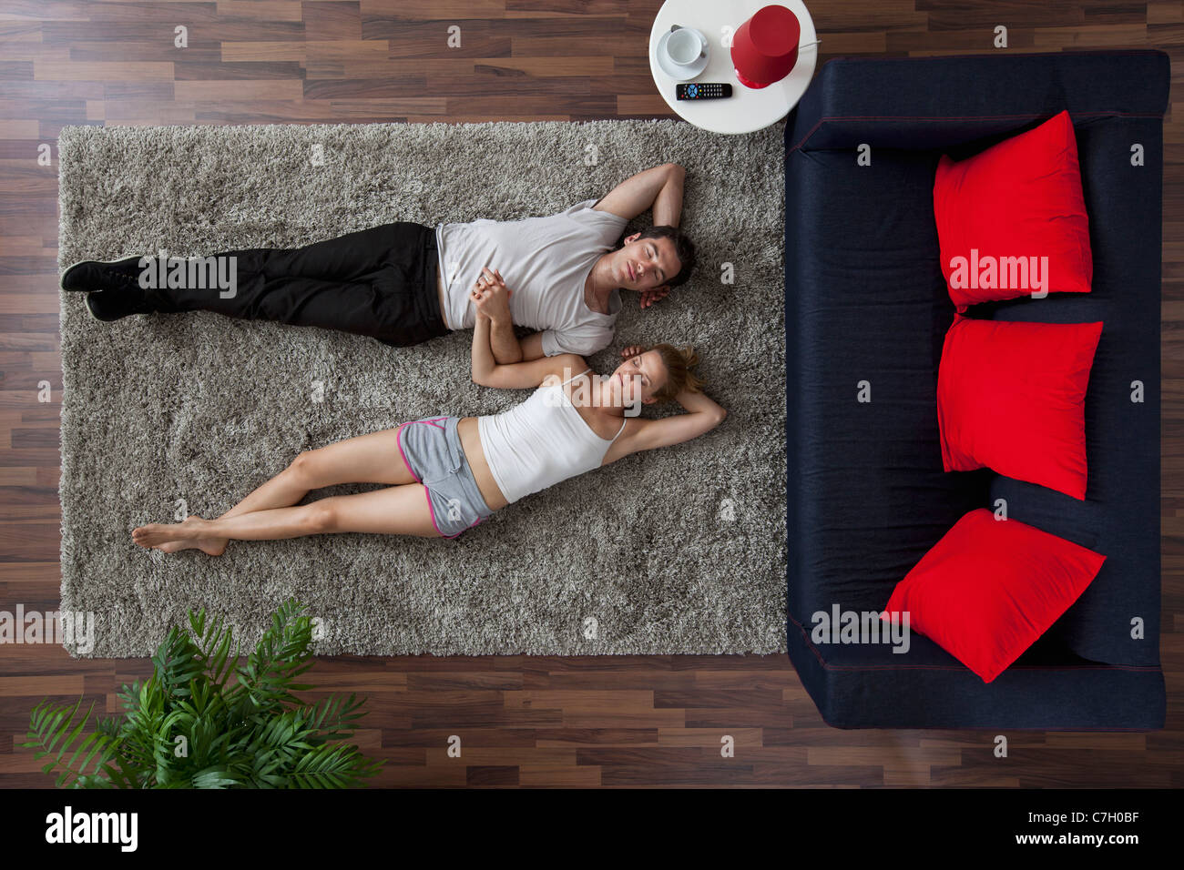 A couple lying on a living room rug, holding hands and sleeping, overhead view Stock Photo