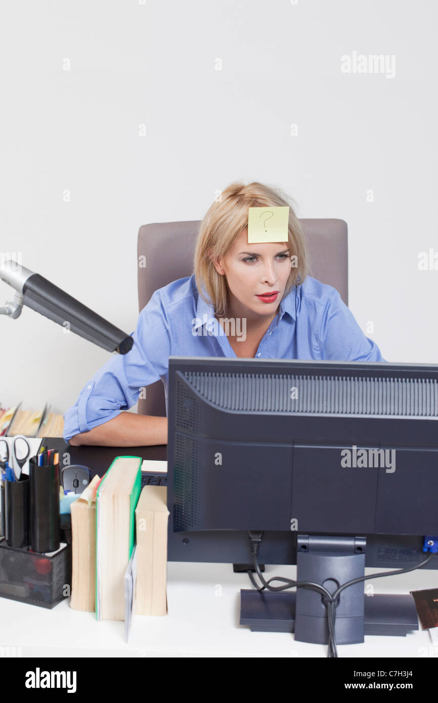 Woman looking at computer with adhesive note stuck on her forehead Stock Photo