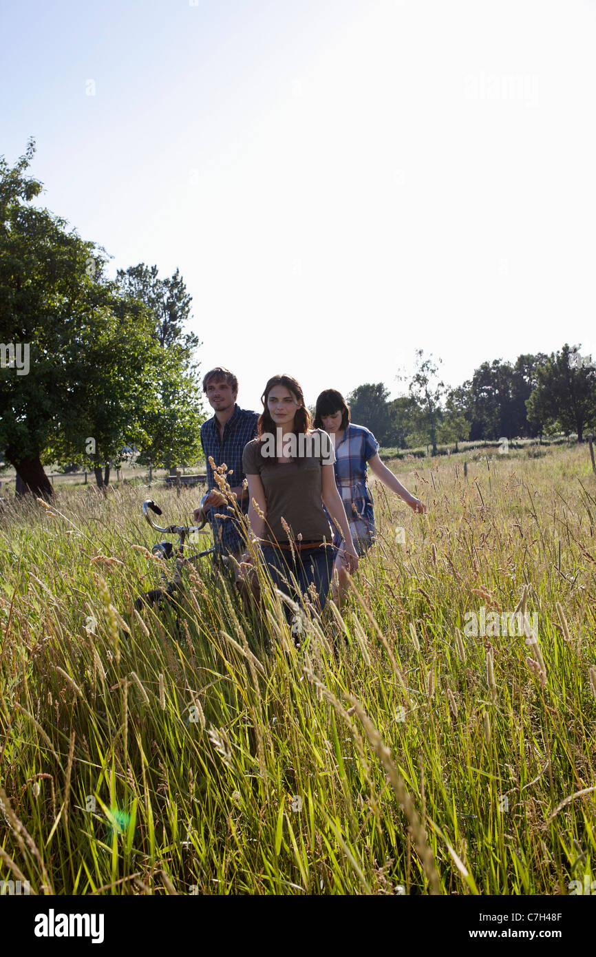 Three friends amongst the timothy grass walk with bike Stock Photo