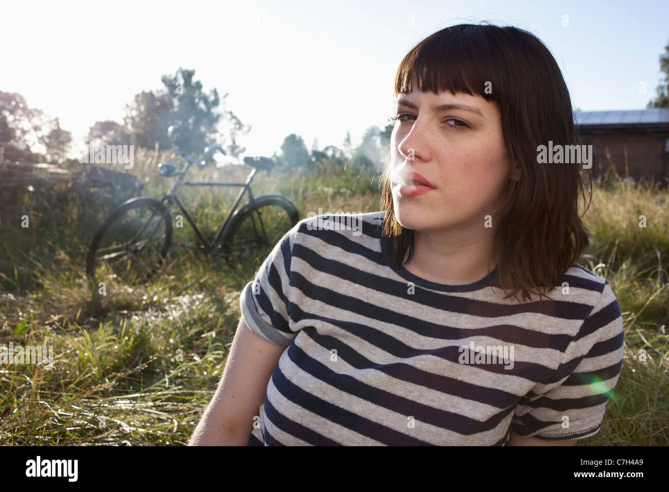 Girl sitting in secluded field exhaling smoke Stock Photo