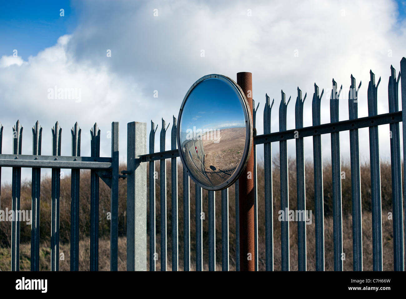A concave mirror on a metal perimeter fence reflects a disused factory site in Workington, Cumbria, England. Stock Photo