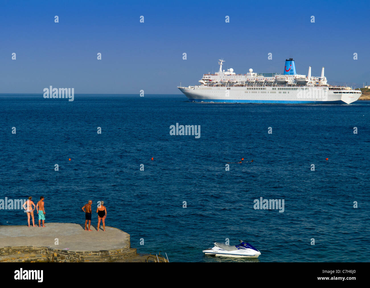 The cruise liner Thomson Spirit leaving the port of Agios Nikolaos on the Greek island of Crete watched by holiday makers. Stock Photo