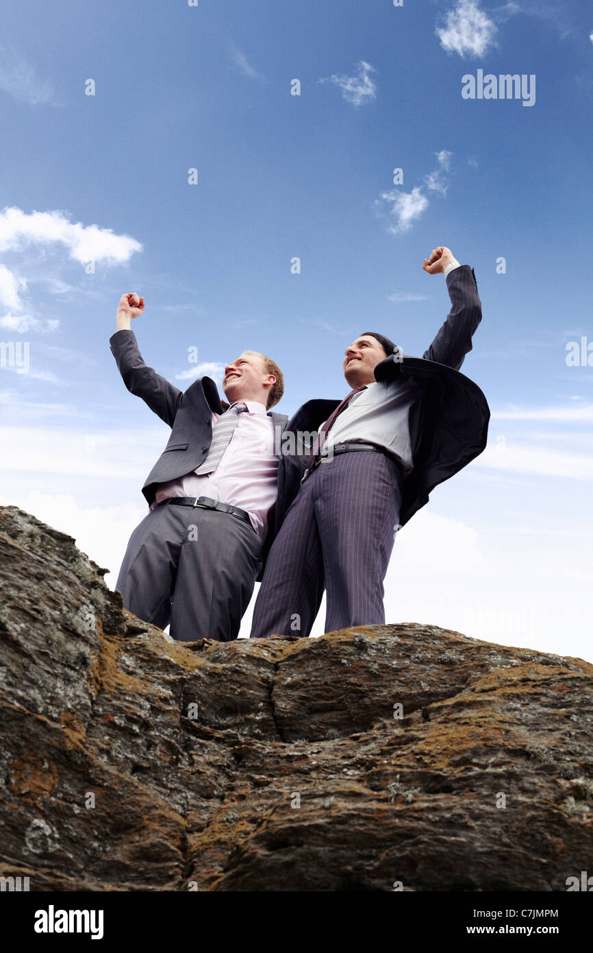 Businessmen cheering on cliff edge Stock Photo