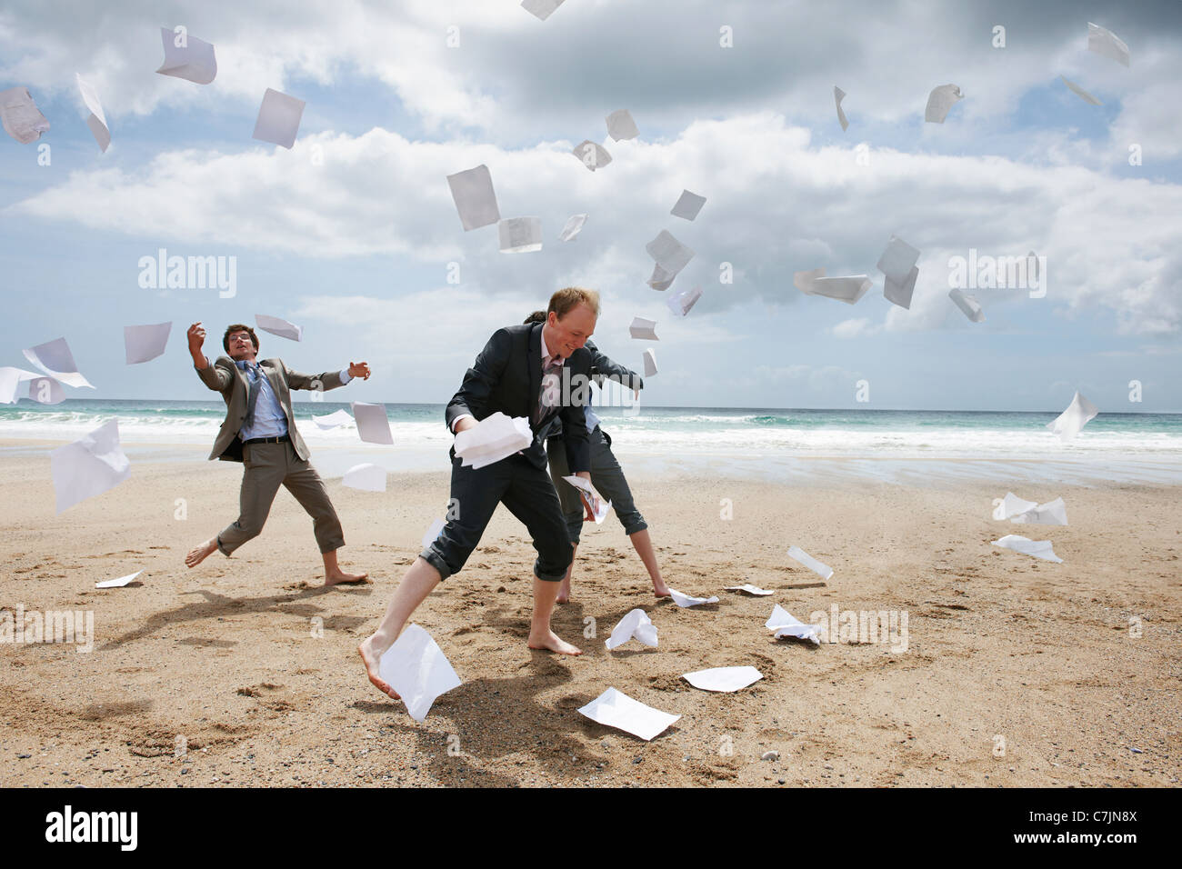 Businessmen tossing papers away at beach Stock Photo