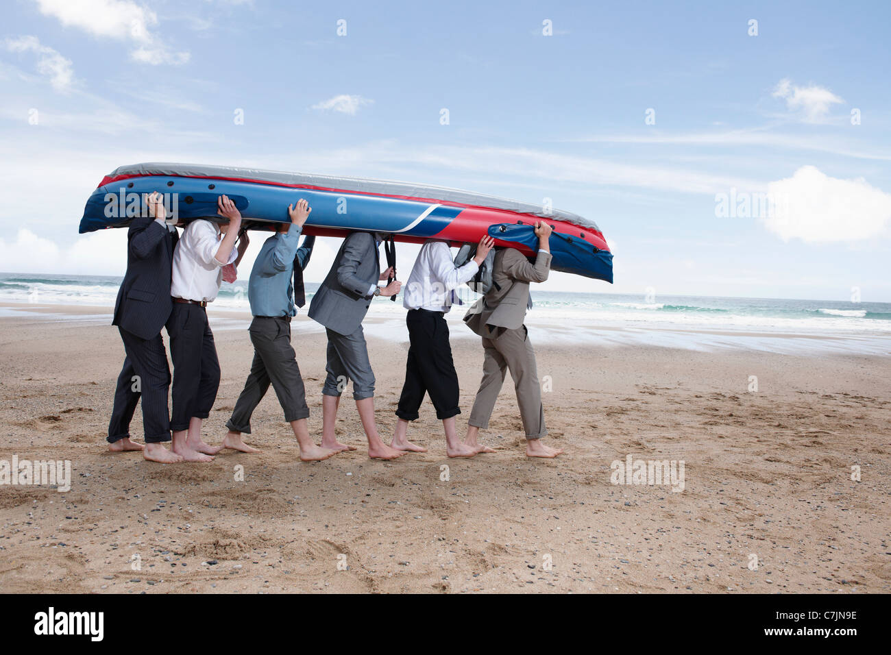 Businessmen carrying canoe on beach Stock Photo