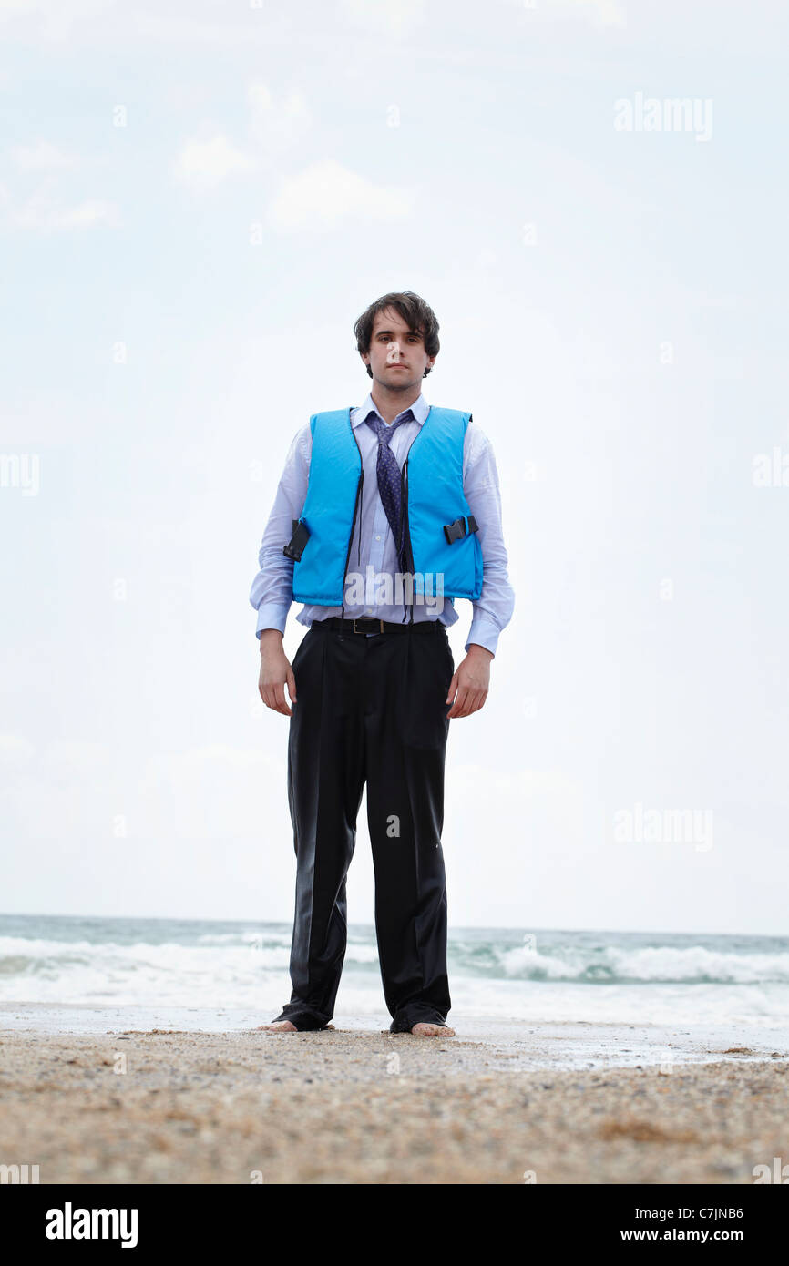 Businessman wearing life jacket on beach Stock Photo