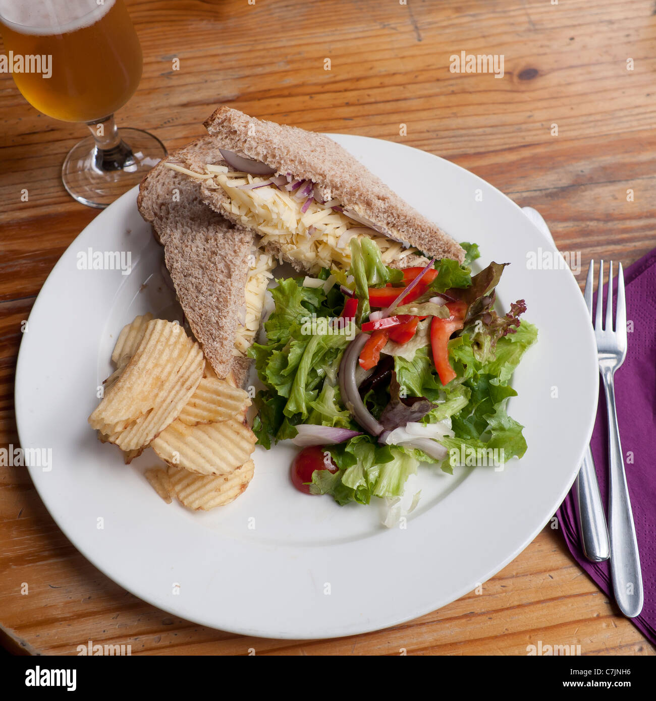 A Cheddar Cheese and red Onion Sandwich with crisps salad and a glass