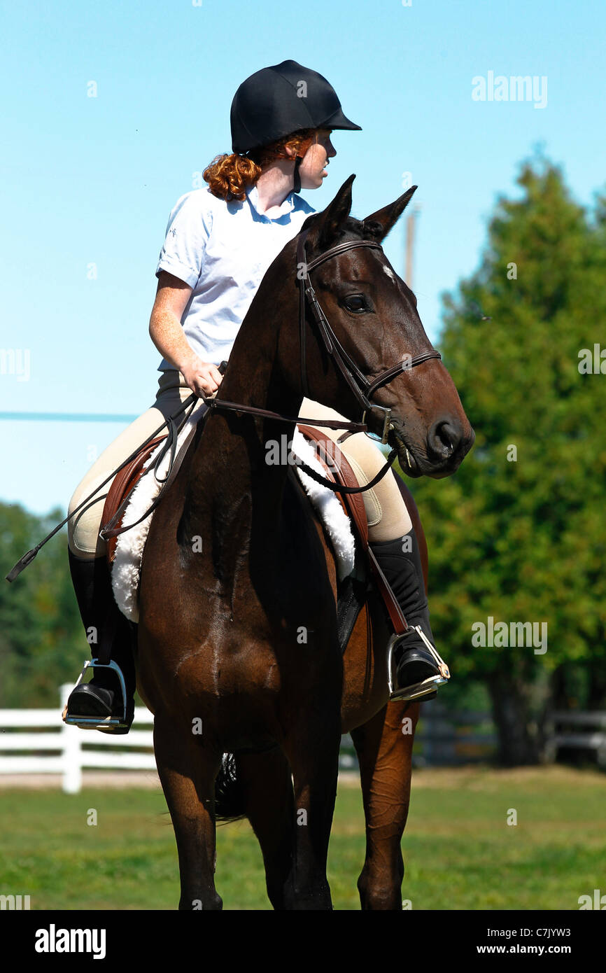 Young girl riding bay horse at a horse show on a summer day Stock Photo